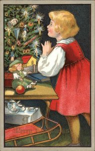 Girl Looks at Gifts Under Christmas Tree Sled Tea Set Doll Vintage Postcard