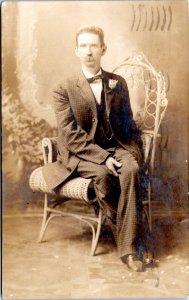 RPPC 1908 Man in suit and bowtie with rose boutonniere sitting on wicker chair