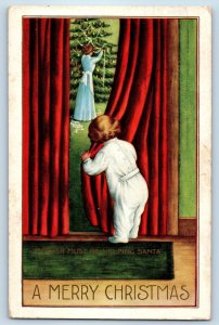 1914 Christmas Child Hiding Mother Must Be Helping Santa Embossed Postcard