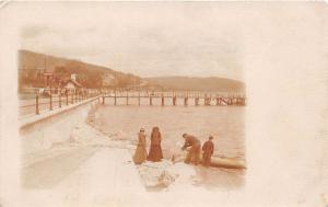 MAN & BOY AT WATER BOAT~2 WOMEN WATCH~PIER IN BACKGROUND UK REAL PHOTO POSTCARD