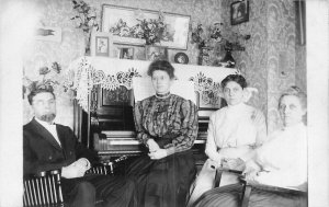 VICTORIAN ERA~WOMEN AND MAN AROUND PIANO IN THE PARLOR~1910 REAL PHOTO POSTCARD