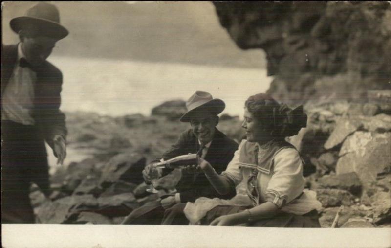 Man & Woman on Rocks Pouring Drink Bottle & Glass c1910 Real Photo Postcard