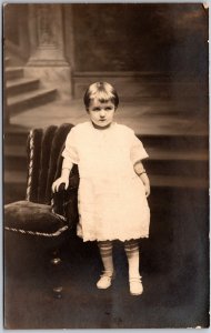 Infant Child in Formal Dress Gown Holds Chair Portrait - Vintage Postcard