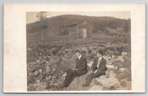 RPPC Two Handsome Men Posing on the Rocks Old Barn in Distance Postcard H26