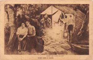 YOUNG COUPLE HIDES FROM GROUP AT CAMP SITE WITH MUSICIANS~ROMANCE POSTCARD 1910