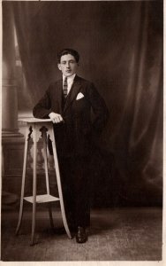VINTAGE POSTCARD RPPC K-LTD (1918-1936) MAN STANDING BESIDE TALL CHAIR STUDIO