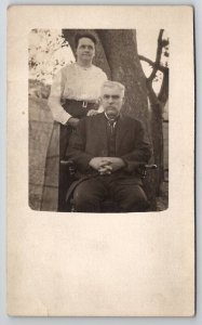 RPPC Older Woman with Man in Chair by Tree c1910  Postcard H28