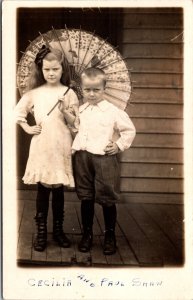 Real Photo Postcard Cecilia and Paul Shaw Two Scowl Faces Paper Umbrella Porch