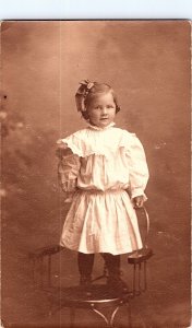 RPPC Postcard of Young Girl White Dress Big Bow Standing on Chair Aristo 1900s