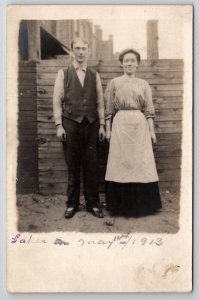 RPPC Woman In Apron And Man Pose In Dirt Yard Wood Fence Postcard M25