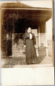 Stoic older woman in black dress standing on porch  Velox 1907-1914 RPPC