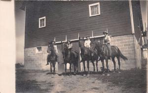 FOUR MEN ON HORSEBACK IN FRONT OF BARN REAL PHOTO POSTCARD c1910s