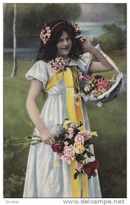 Girl wearing white dress with yellow bow holding wild flowers in basket and b...