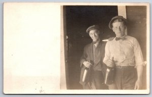 Two Men In Bow-Ties Each Hold Whiskey Bottles~Eyeglasses~Newsboy Cap~c1910 RPPC