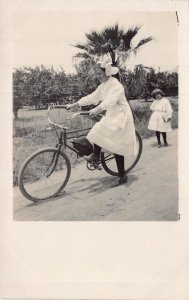 YOUNG GIRL IN WHITE DRESS RIDING BICYCLE ON SANDY ROAD~1910s REAL PHOTO POSTCARD