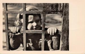 YOUNG GIRL LOOKING THROUGH HEAVY METAL GATE-GERMAN PHOTO POSTCARD