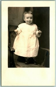 RPPC Adorable Smiling Baby Standing On Chair Wearing White AZO Postcard H5