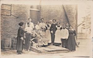 WOMAN INSTRUCTING HOTEL EMPLOYEES-BELL BOY CAP ON YOUNG MAN-REAL PHOTO POSTCARD