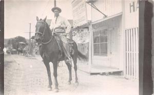 MAN WEARING HAT & TIE SEATED ON HORSE IN BUSINESS AREA-REAL PHOTO POSTCARD 1900s