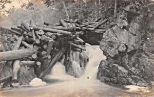 MAN SITTING ON DAM OF LARGE LOGS~SMALL WATERFALL~REAL PHOTO POSTCARD1910s