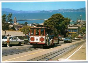 Cable Car climbing hill with sailboats in bay in background, San Francisco