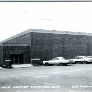 c1960s Oelwein, IA RPPC Sacred Heart Gymnasium Postcard Dodge Coronet Vtg A102