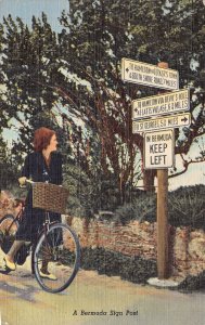 BERMUDA~WOMAN RIDING BICYCLE LOOKS AT SIGN POST~1951 POSTCARD