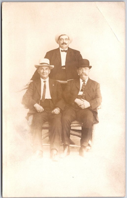 Three Men Sitting On Chair Mustache Black Suit Real Photo RPPC Postcard