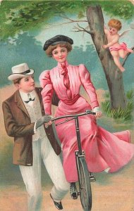 FINELY DRESSED COUPLE-CUPID WATCHES ROMANTIC BICYCLE LESSON~1910s POSTCARD