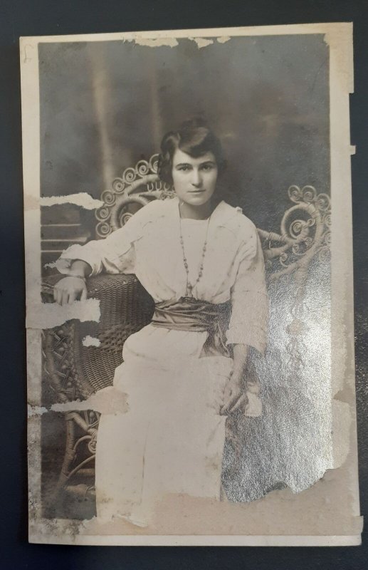 RPPC Pretty woman seated in fancy rattan chair - damaged