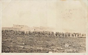 UNITED STATES WW1 SOLDIERS WORK IN FIELD IN FRONT OF BARRACKS-RPPC POSTCARD