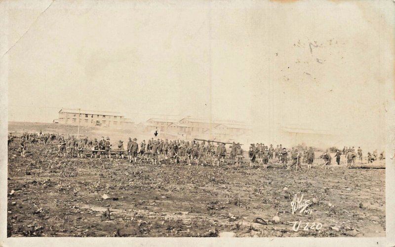 UNITED STATES WW1 SOLDIERS WORK IN FIELD IN FRONT OF BARRACKS-RPPC POSTCARD