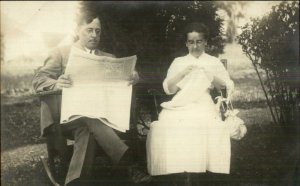 Couple in Chairs Man Reading Newspaper Woman Embroidering c1910 RPPC