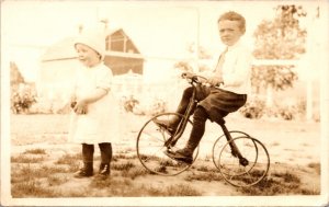 Real Photo Postcard Toddler Girl and Young Boy on a Tricycle in Yard Garden