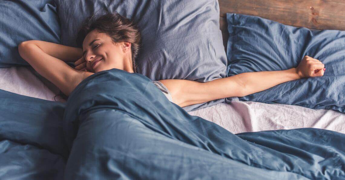 Happy young woman waking up stretching in bed