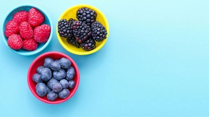 Blueberries, raspberries and blackberries in 3 small yellow bowls