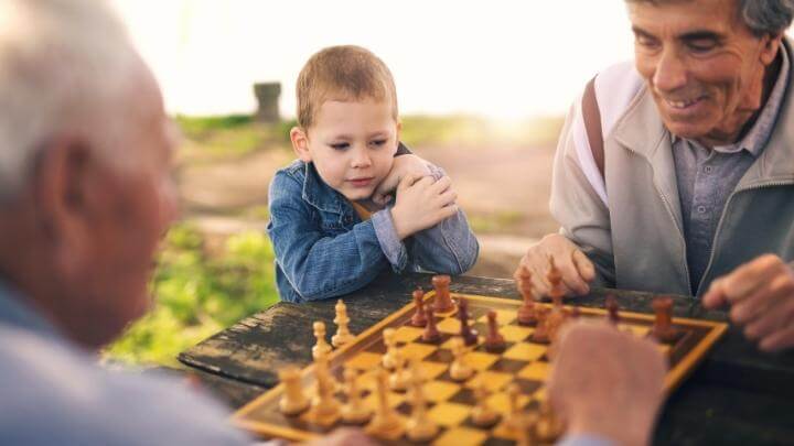 A young child watching his grandfather play chess with a friend