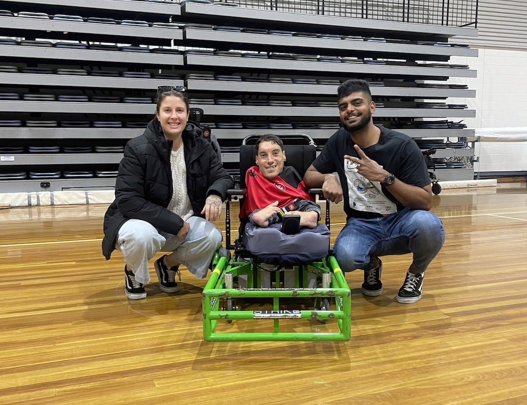 Abdullah is sitting in his lime green powerchair between two people crouching. 
