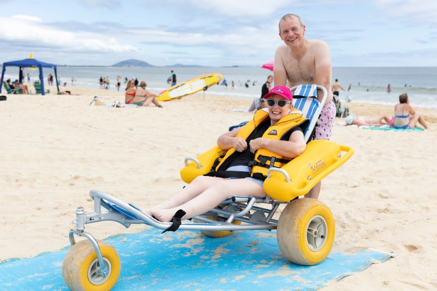 Woman using a beach wheelchair at the beach with a carer