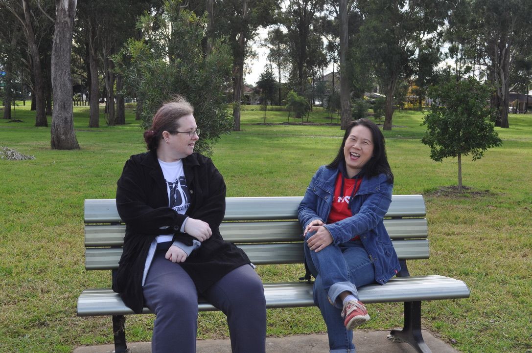 An NDIS support worker and her client sitting on a park bench