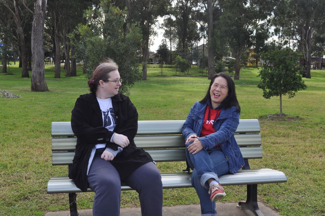 A disability support worker with a client sitting on a bench