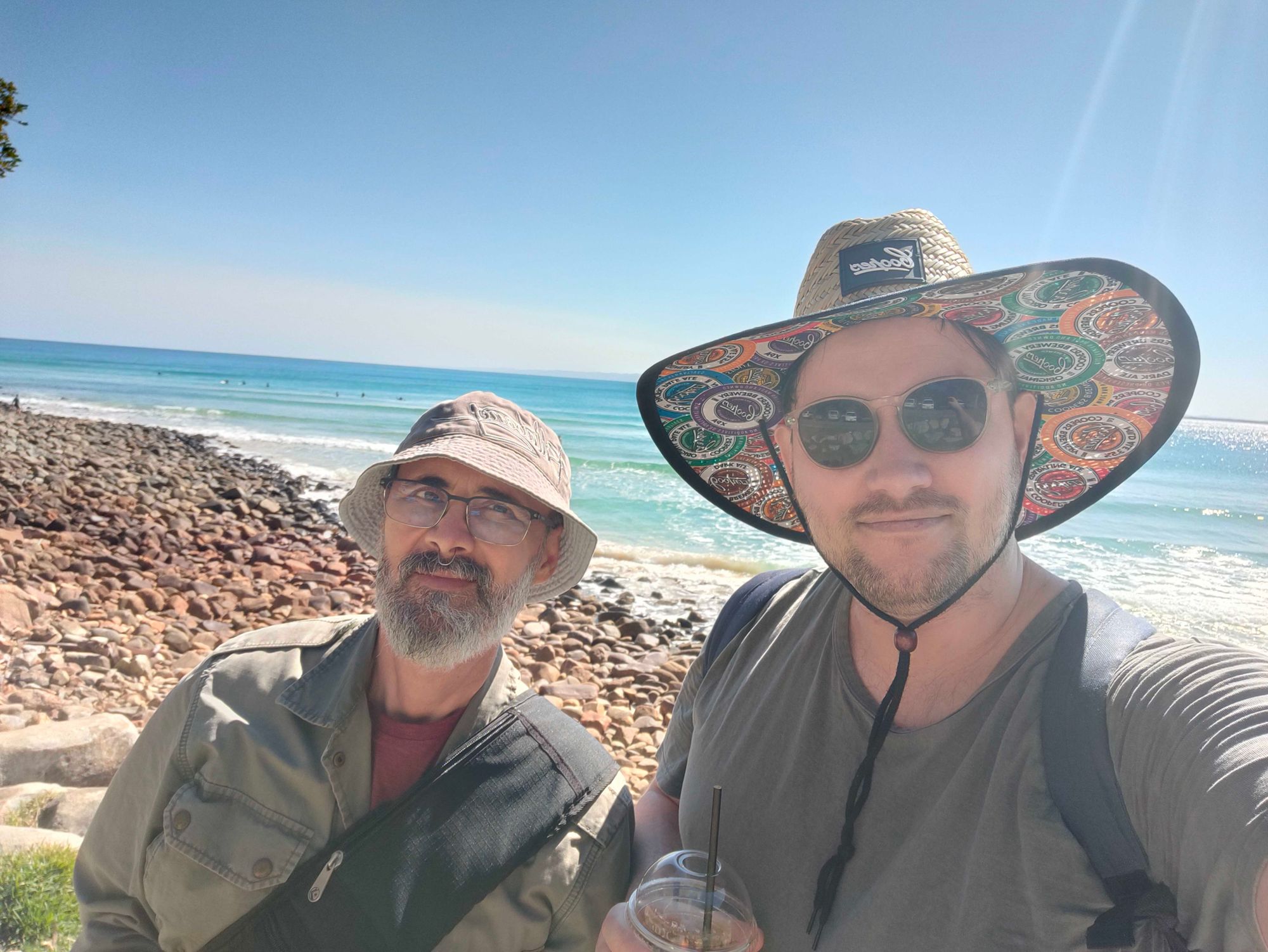 Two men wearing wide brim hats take a selfie at the beach