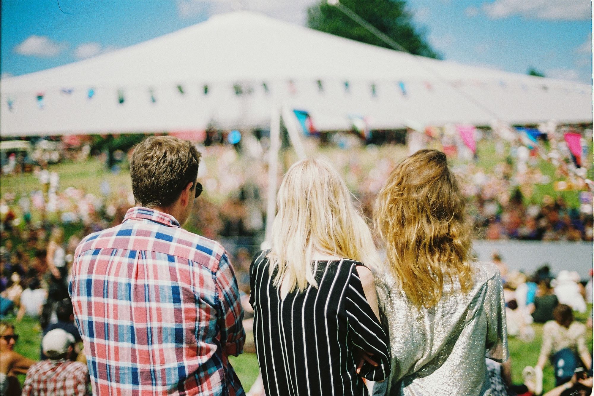 3 people at a festival outdoors, looking at a tent