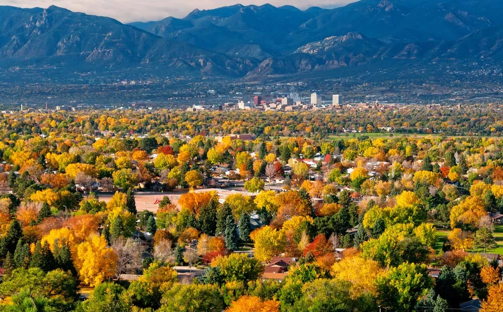 picture of Monument Colorado's landscape with red, green, yellow trees in the foreground, mountains in the background