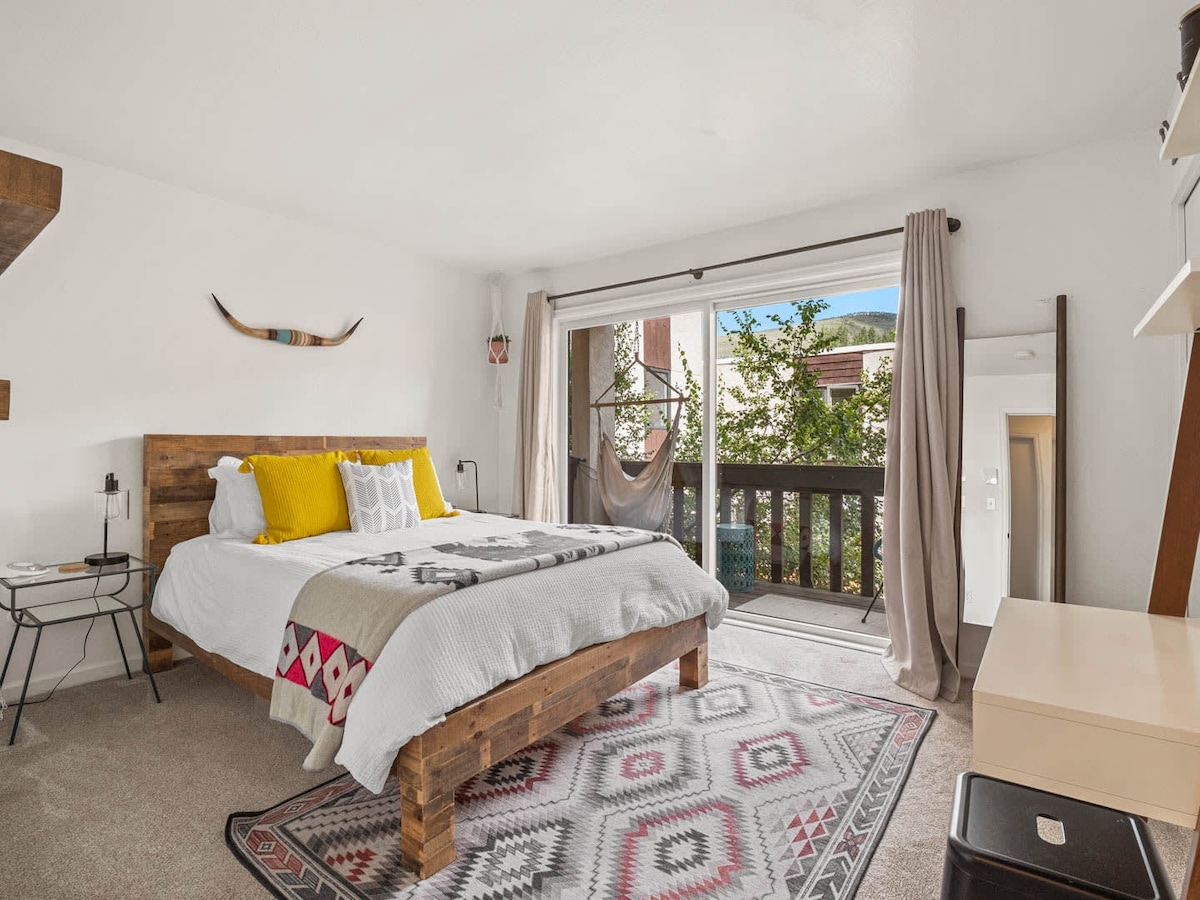 Bedroom shown with bed made and window/balcony to the right. White sheets and colorful runner