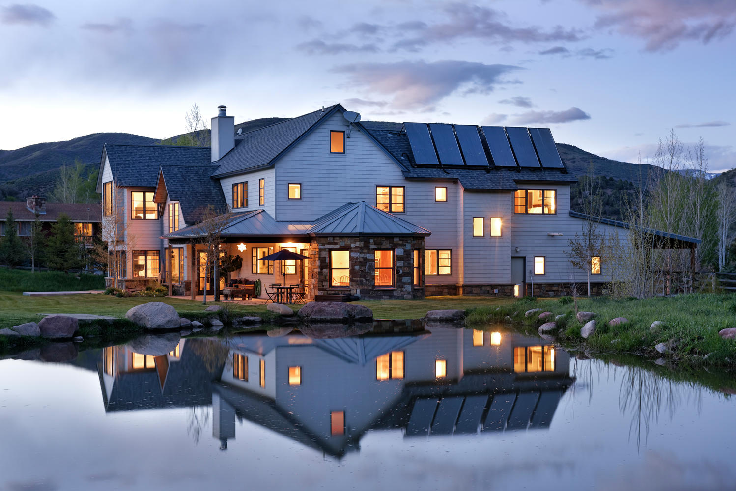 House shown with a pond out front reflecting the house. Mountains and sky in the background