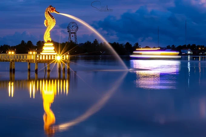 Illuminated seahorse statue fountain on the Kampot riverside at dusk with light trails from a boat