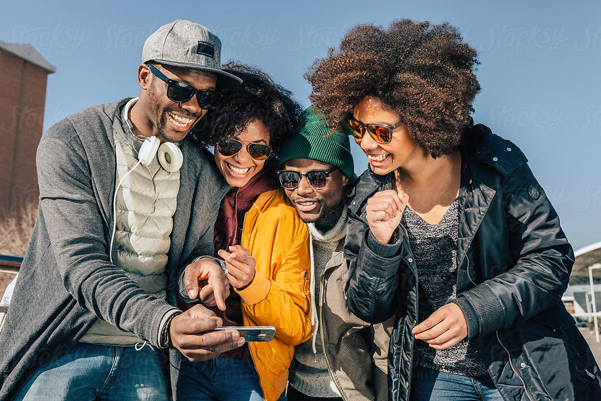 Group of stylish young Black friends laughing and looking at a smartphone together outdoors, embodying a cool urban app vibe.