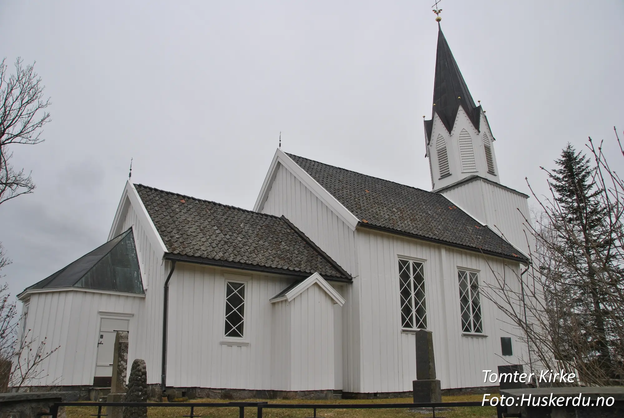 Tomter kirke, en tradisjonell langkirke i Indre Østfold, Østfold fylke, er bygget i tømmer og har en rik historie som strekker seg tilbake til 1600-tallet. Kirken er kjent for sin nygotiske altertavle fra 1880 og vakre kirkegård, som reflekterer områdets kulturarv. Foto: Huskerdu.no