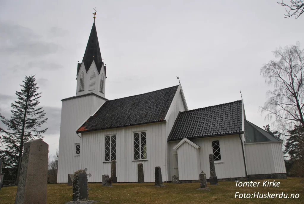 Tomter kirke, en tradisjonell langkirke i Indre Østfold, Østfold fylke, er bygget i tømmer og har en rik historie som strekker seg tilbake til 1600-tallet. Kirken er kjent for sin nygotiske altertavle fra 1880 og vakre kirkegård, som reflekterer områdets kulturarv. Foto: Huskerdu.no
